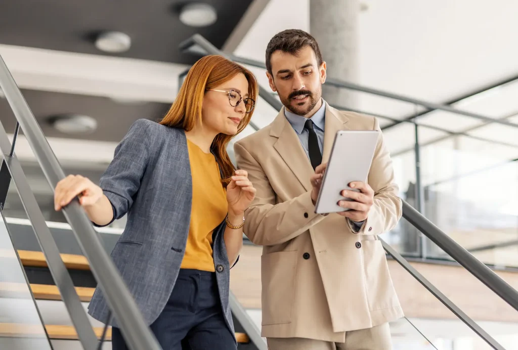Businesspeople descending stairs at corporate office and looking at the tablet.